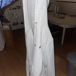 Grå hoodie från Ralph Lauren - Säljer en stilren grå hoodie från Ralph Lauren med dragkedja och det klassiska logotypbroderiet på bröstet. Perfekt för en avslappnad look.