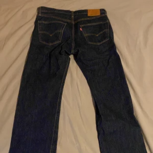 Mörkblå jeans från Levi's W33 L34 - Snygga mörkblå jeans från Levi's med klassisk femficksdesign och knappgylf. Perfekta för en avslappnad stil. De har en rak passform och är tillverkade i slitstarkt denim. Inga skador eller liknande och knappast använda. 