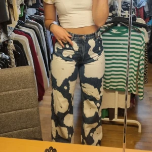 Blå och vita jeans med unikt mönster - Säljer ett par coola blå jeans med ett unikt vitt mönster. De har en klassisk femficksdesign och är tillverkade i 100% bomull. Perfekta för dig som vill sticka ut med en unik stil!
