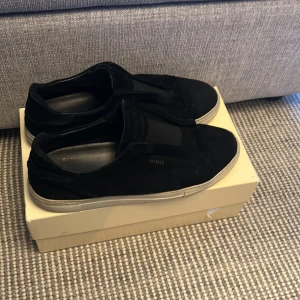 Arigato skor - Snygga svarta loafers i mocka med en stilren design. Skorna har en vit sula som ger en fin kontrast till det svarta. Perfekta för en avslappnad men ändå elegant look.
