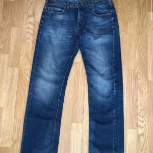  Lee Straight Jeans  - Säljer ett par klassiska blå jeans från Lee med knappgylf och femficksdesign. Perfekta för en avslappnad stil.