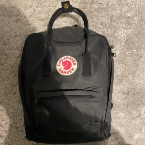 Svart ryggsäck från Fjällräven Kånken - Säljer en klassisk svart Fjällräven Kånken ryggsäck. Den har en praktisk dragkedja och ett ikoniskt rundat märke på framsidan. Perfekt för vardagsbruk med ett rymligt huvudfack och en mindre framficka. Mått: Höjd 36 cm, bredd 27,5 cm, djup 12cm.