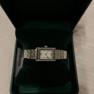 Silverfärgad klocka från Ivy N Rox - Elegant silverfärgad klocka från Ivy N Rox med rektangulär urtavla och romerska siffror. Klockan har en länkarmband och är inramad med glittriga stenar. Perfekt för att ge en touch av lyx till din stil. Klockan är helt oanvänd och har fortfarande plasten, samt lappen kvar. Du som köper kan korta klockan efter din passform kostnadsfritt hos Ur&Penn. Pris kan diskuteras:)