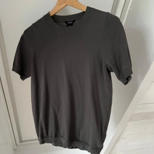 Grå kortärmad tröja från Lindex - Säljer en finstickad grå T-shirt från Lindex. Den är kortärmad med rund halsringning och ribbade kanter. Knappt använd!