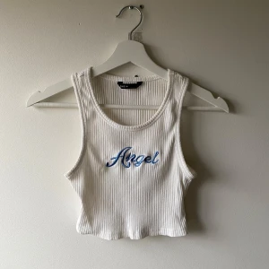 Vit ribbad linnetopp  - Säljer en vit ribbad linnetopp med texten 'Angel' broderad i blått på framsidan. Toppen är croppad.