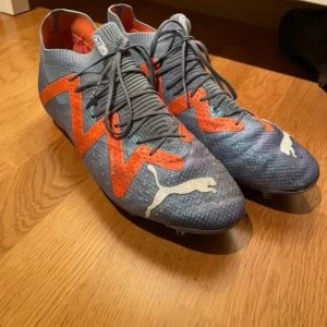 Fotbollsskor från Puma - Snygga fotbollsskor från Puma i grått och orange med snörning. Skorna har en modern design med tydliga logotyper och en slitstark sula för bra grepp på planen. Köptes för 2599, priset kan alltid diskuteras vid snabb affär. 