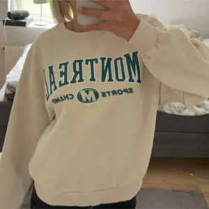 Beige sweatshirt från Gina Tricot - Säljer en beige sweatshirt från Gina Tricot med texten 'Montreal Sports Champ' i blått på framsidan. Tröjan har en rund halsringning och långa ärmar. Perfekt för en avslappnad stil.