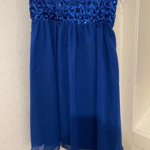 Blå paljettklänning från Vila - Snygg blå klänning från Vila med paljetter på överdelen och tunna axelband. Kjoldelen är i ett lätt och flödande material som ger en fin siluett. Perfekt för festliga tillfällen! Klänningen är oanvänd och i mycket bra skick. Priset kan diskuteras. 