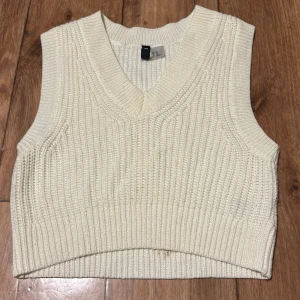 Vit stickad väst från Divided - Säljer en stilren vit stickad väst från Divided. Västen har en v-ringad design och är croppad, vilket ger en modern look. Perfekt för lager-på-lager-stil under svalare dagar.