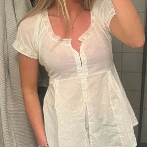 Vit blus med spetsdetaljer - Säljer en söt vit blus med korta ärmar och rund halsringning. Blusen har fina rynkade detaljer vid ärmslut och hals. Perfekt för en somrig look!
