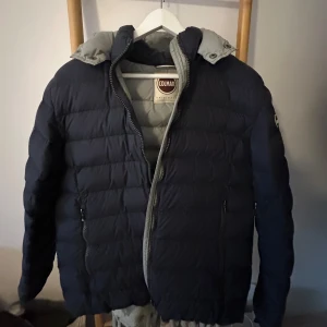 Mörkblå dunjacka från Colmar - Säljer en snygg mörkblå dunjacka från Colmar. Jackan har en quiltad design med dragkedja och en praktisk huva. Storlek 50
