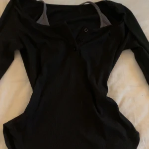 Svart långärmad topp - Säljer en stilren svart långärmad topp med knappar framtill. Perfekt för en enkel och snygg look. Den har inbyggd halterneck detalj också!