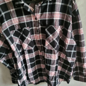 Rutig skjorta från H&M Divided - Snygg rutig skjorta från H&M Divided i svart, vit och röd. Skjortan har långa ärmar och knappar framtill. Perfekt för en avslappnad stil med två bröstfickor för extra detaljer.