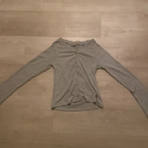 Grå ribbad kofta med knappar - Säljer en stilren grå ribbad kofta från Ü. Den har långa ärmar och knappar framtill, perfekt för lager-på-lager-stil. Passar både till vardags och mer avslappnade tillfällen.
