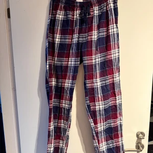 Rutig pyjamas byxa från Time to Lounge - Mysiga rutiga byxor i blått, rött och vitt från Time to Lounge. De har en bekväm resårmidja med snörning för justerbar passform. Perfekta för en avslappnad dag hemma.