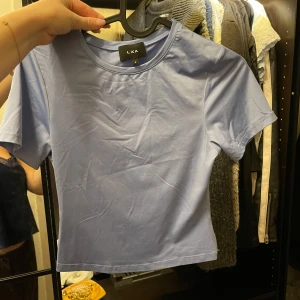 Ljusblå t-shirt från LXA - Säljer en ljusblå t-shirt från LXA. Tight i modellen och SUPERskönt material 