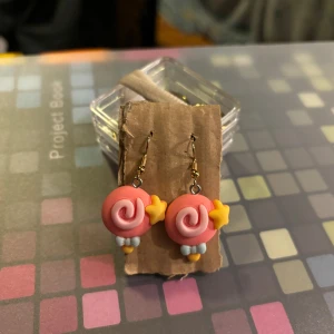 Färgglada örhängen med snurrdesign - Charmiga örhängen med en lekfull snurrdesign i rosa och gult. De har små stjärndetaljer och hänger från en enkel krok. Perfekta för att lägga till en färgglad touch till din outfit.