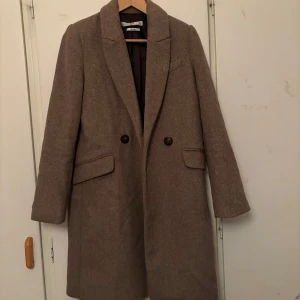 Beige kappa med knappar - Snygg beige kappa från Mango med klassisk design. Den har långa ärmar och två stora knappar framtill. Perfekt för höst och vår, med en stilren look som passar till många outfits.