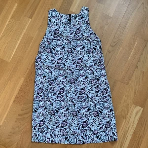 Mönstrad klänning från Zoul Edition - Snygg ärmlös klänning från Zoul Edition med ett abstrakt mönster i svart, rosa och ljusblått. Perfekt för en stilren look med sin enkla design och bekväma passform. Fodrad och med dragkedja bak. 