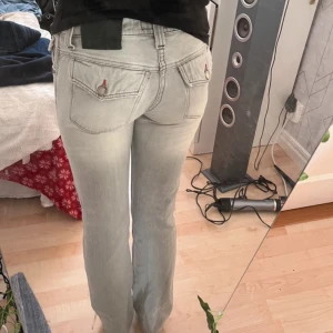 Ljusblå jeans med bootcut - Snygga ljusblå jeans med bootcut-stil och klassisk femficksdesign. De har en låg midja och är perfekta för en avslappnad look. Märket är inte specificerat, men de har en stilren design med dekorativa sömmar.