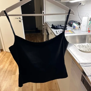 Svart axelbandslös topp - Snygg svart axelbandslös topp med smala axelband och en stilren design. Perfekt för en kväll ute eller som en del av en lager-på-lager-look.
