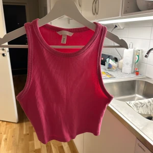 Rosa ribbad linnetopp från H&M - Säljer en snygg rosa ribbad linnetopp från H&M. Toppen är ärmlös och croppad, perfekt för varma sommardagar. Den har en rund halsringning och är gjord i ett mjukt material.