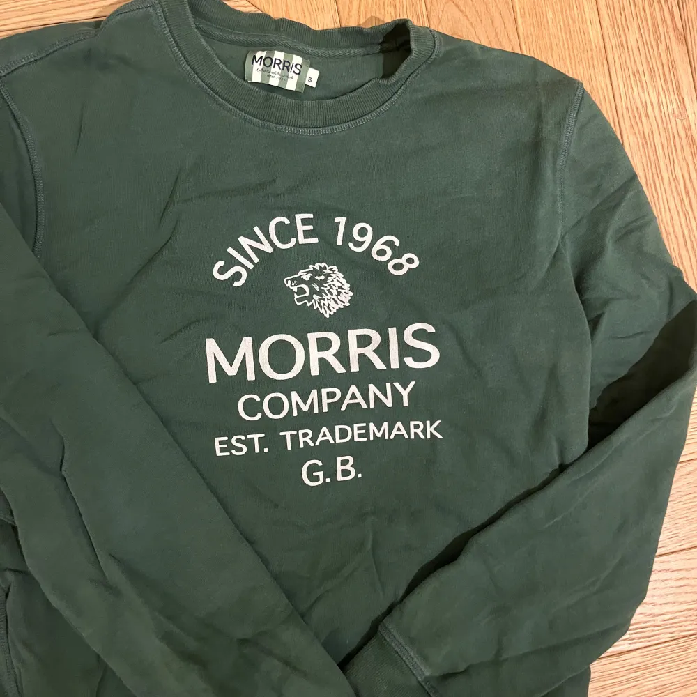 Säljer en grön tröja från Morris med tryck framtill. Tröjan har långa ärmar och rund halsringning. Perfekt för en avslappnad stil.. Neuletakit & Villapaidat.