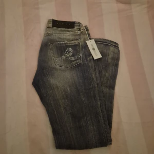 Grå/blå jeans från Ross Disera - Snygga grå jeans från Ross Disera med slitna detaljer och broderade bakfickor. Perfekta för en avslappnad stil med en touch av edge. Jeansen är helt nya aldrig använda köpte av en min för de passa inte henne o säljer för de är tyvärr för stora för mig. Måtet på midlands rakt över är 37cm och rakt över låret 21cm. Ben längden är 98cm. Skriv om ni har frågor