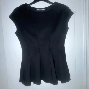 Svart topp från Gina Tricot - Snygg svart topp från Gina Tricot med korta ärmar och en lätt utsvängd nederdel. Perfekt för en stilren look.