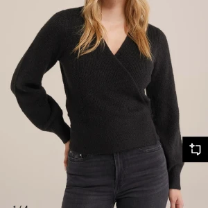 Svart omlottkofta från Gina  - Snygg svart knitted wrap cardigan från Gina tricot i mjukt material. Koftan har långa ärmar och knytning i midjan för en stilren look. Perfekt för kyligare dagar. Prislappen är kvar