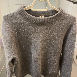 Grå stickad tröja - Säljer en mysig grå stickad tröja med rund halsringning. Perfekt för kyliga dagar med sin mjuka och bekväma passform. Tröjan har en enkel design som gör den lätt att matcha med olika outfits.