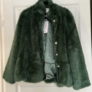 Grön fuskpälsjacka från Derby - Helt ny! Aldrig använd. Storlek L. Lyxig grön fuskpälsjacka från Derhy. Jackan har en mjuk och fluffig yta med knappar framtill. Perfekt för att hålla sig varm och stilren under kyliga dagar. 🌿nypris 1995kr. Porto tillkommer. Kan lämnas i Stenungsund eller Göteborg. 
