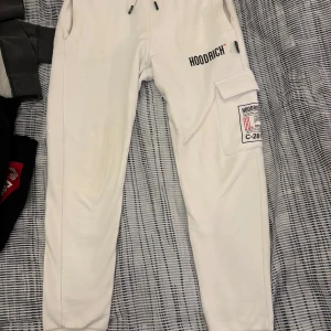 Vita mjukisbyxor från Hoodrich - Snygga vita mjukisbyxor från Hoodrich med tryck på benet och en praktisk ficka på sidan. Byxorna har snörning i midjan och är perfekta för en avslappnad stil.