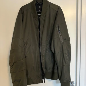 Olivgrön bomberjacka från G-Star RAW - Snygg olivgrön bomberjacka från G-Star RAW med dragkedja framtill och en praktisk ficka med dragkedja på ärmen. Jackan har en klassisk bomberstil med ribbade muddar vid ärmslut och nederkant.
