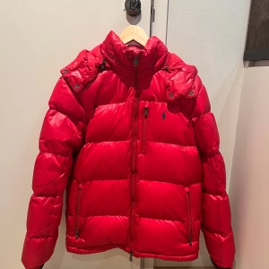 Röd dunjacka från Ralph Lauren - Snygg röd dunjacka från Ralph Lauren med dragkedja och huva. Jackan har långa ärmar och en liten logotyp på bröstet. Perfekt för kalla dagar. Köpt i Täby centrum på Thernlunds och är köpt för 6999 kr. Den är storlek S i vuxen storlek. DM mig om du är intresserad av att köpa! Den är bara använd förra vinter och är som i ny skick, så väldigt ny.❤️Om ni vill ha mer bilder så kan jag skicka hur den ser ut på.