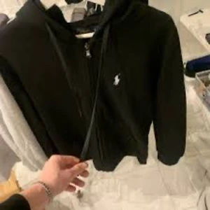 Ralph Lauren hoodie svart - Snygg svart hoodie från Polo Ralph Lauren med dragkedja och klassisk logga på bröstet. Perfekt för en avslappnad stil.