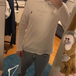 Vit hoodie från Ralph Lauren - Säljer en stilren vit hoodie från Ralph Lauren med en liten broderad logga på bröstet. Tröjan har långa ärmar och en justerbar huva med snörning. Perfekt för en avslappnad look.