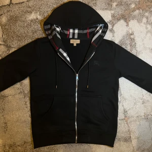 Burberry - Säljer en snygg svart hoodie från Burberry med klassiskt rutigt mönster i huvan. Har aldrig använt den pga den var för liten för mig. Köpte den för 4800 från Liverpool i England. Pris kan diskuteras