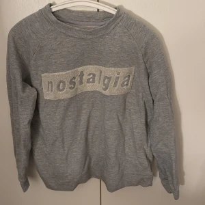 Grå sweatshirt från Samsøe Samsøe - Säljer en grå sweatshirt från Samsøe Samsøe med texten 'nostalgia' i ett glittrigt tryck på framsidan. Står inte storleken på tröjan men skulle säga att den är i storlek xs/s🫶🏻