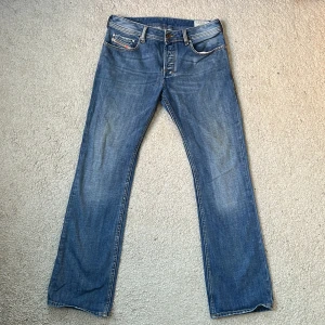 Blå jeans från Diesel - Säljer ett par klassiska blå jeans från Diesel, modell Zatiny. De har en rak passform med fem fickor och knappgylf. Perfekta för en avslappnad stil.