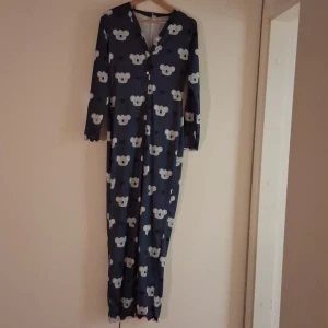 Marinblå overall pyjamas med koalas och hjärtor på - Oanvänd Marinblå overall pyjamas med söta kalas och hjärtan på. Handleden har ljusrosa vågig sömn. Overallen är 170 cm.