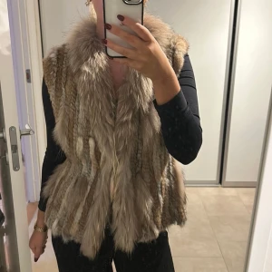 Beige pälsväst - Säljer en snygg beige pälsväst som är perfekt för att hålla sig varm och stilren. Västen har en naturlig look med mjuk päls och är lätt att matcha med olika outfits.