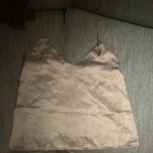 Beige, grå sidenlinne från Black Label Collection - Säljer ett elegant beige linne från Black Label Collection i sidenmaterial. Linnet har tunna axelband och en stilren design, perfekt för en chic look. Aldrig använt.