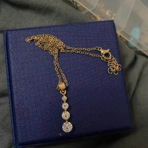 Guldhalsband med glittriga detaljer - Elegant guldhalsband med en kedja och hängsmycke bestående av flera glittriga stenar. Perfekt för att ge en touch av glamour till din outfit.