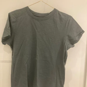 Grön t-shirt från Kappahl - Säljer en enkel och stilren grå t-shirt från Kappahl. Perfekt för en avslappnad look. T-shirten har en rund halsringning och korta ärmar.