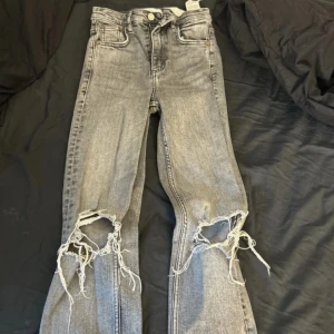 Grå jeans med slitningar - Snygga grå jeans med coola slitningar på knäna. Perfekta för en avslappnad och trendig look. De har en klassisk femficksdesign, använda men som nya, har även klippt lite där nere men de passar folk mellan 150-167/8