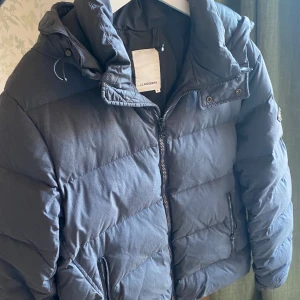 Mörkgrå jacka från J.Lindeberg - Säljer en stilren pufferjacka från J.Lindeberg. Jackan har en praktisk dragkedja och en mysig huva. Perfekt för kyliga dagar med sin quiltade design och långa ärmar. Storleken är XL, personen på bilden är 185cm.Fraktas spårbar eller hämtas i Stockholm. Nypris = 3599kr 
