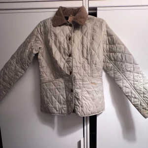Barbour jacka i beige  - Säljer en snygg beige  jacka från Barbour med knappar och krage i kontrastfärg. Jackan har långa ärmar och praktiska fickor. 