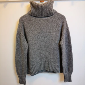 Grå tröja i 100 % Kashmir från Lisa Yang modell Lucca S/M - Grå tjock stickad tröja med hög krage i 100 % Kashmir från Lisa Yang modell Lucca. Mysig grå polotröja med ribbstickade detaljer vid krage, ärmslut och nederkant. Perfekt för kyliga dagar med sin varma och bekväma design. Nypris 5900kr. Storlek 0 motsvarar S/M. 