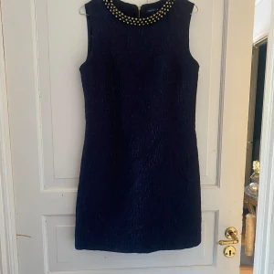 Mörkblå klänning från Stockh LM 36 - Elegant mörkblå klänning från Stockh LM med glittrande detaljer runt halsringningen. Klänningen har en stilren design med en dragkedja baktill och är ärmlös. Perfekt för en kväll ute eller en speciell tillställning.